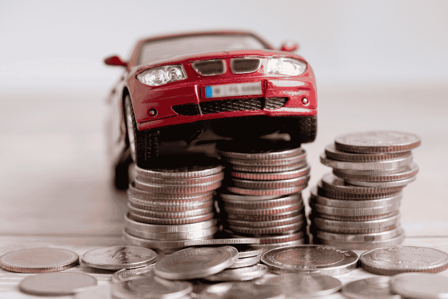 Miniatura de carro vermelho sobre pilhas de moedas representando a revenda lucrativa de veículos comprados em leilão