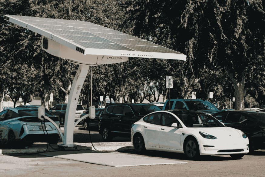 Carro elétrico branco recarregando em estação solar, representando economia e custo de carregamento no Brasil em 2025.
