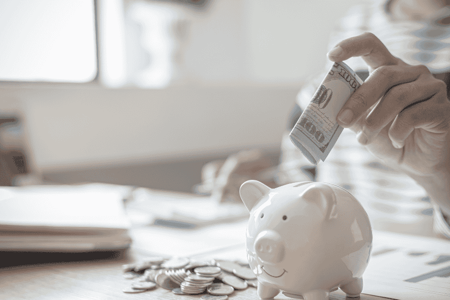Mão colocando dinheiro em cofrinho de porquinho, simbolizando economia no seguro do carro com escolhas conscientes.