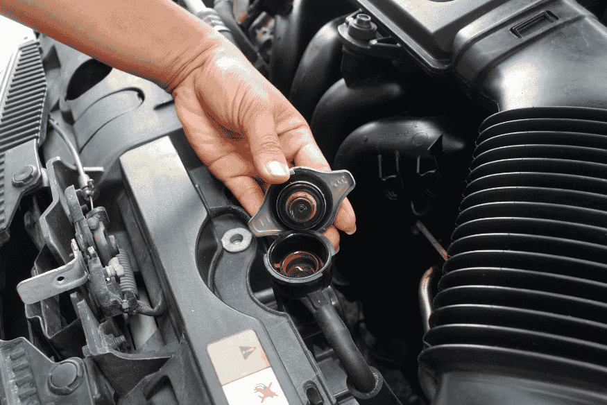 Mão abrindo a tampa do radiador de um carro, evidenciando a manutenção do sistema de arrefecimento automotivo.