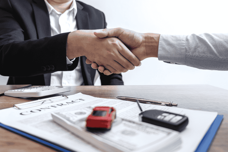 Negociação de financiamento de carro em 2025 com contrato, chaves e aperto de mãos.