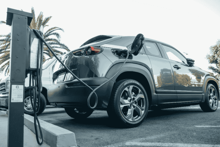 Carro elétrico cinza conectado a ponto de recarga urbano, representando o avanço da infraestrutura em grandes cidades brasileiras em 2025.
