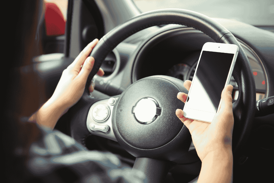 Motorista segurando celular enquanto dirige, representando o uso do celular ao volante e o risco de multas de trânsito no Brasil.