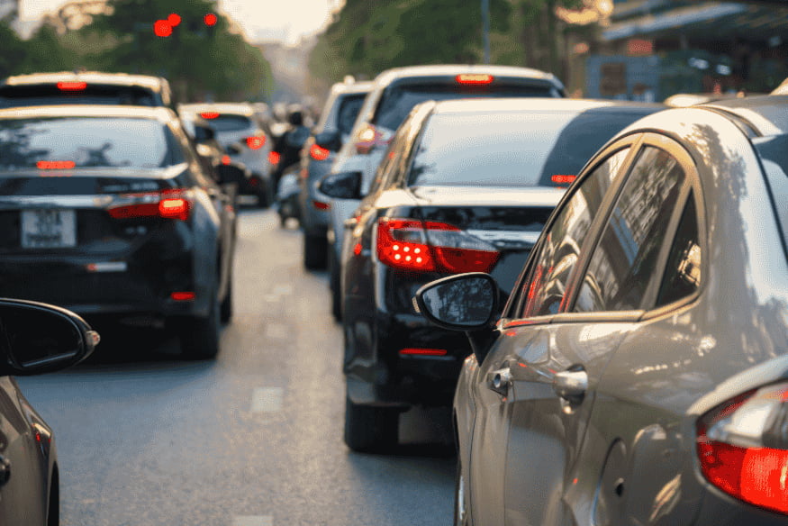 Trânsito intenso em avenida com vários carros parados no sinal vermelho, representando infrações comuns e cuidados no trânsito em 2025.