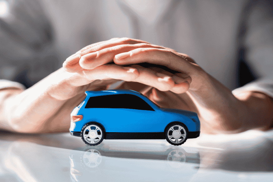 Mãos protegendo miniatura de carro azul, simbolizando a importância do seguro para carros elétricos em 2025.