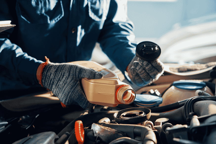 Mecânico realizando troca de óleo em motor de carro, usando óleo lubrificante para manutenção preventiva e aumento da durabilidade do motor.