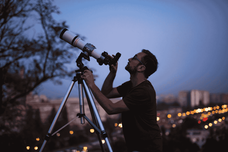Astrônomo ajustando telescópio em tripé ao anoitecer, preparando equipamento para autoguiding na astrofotografia