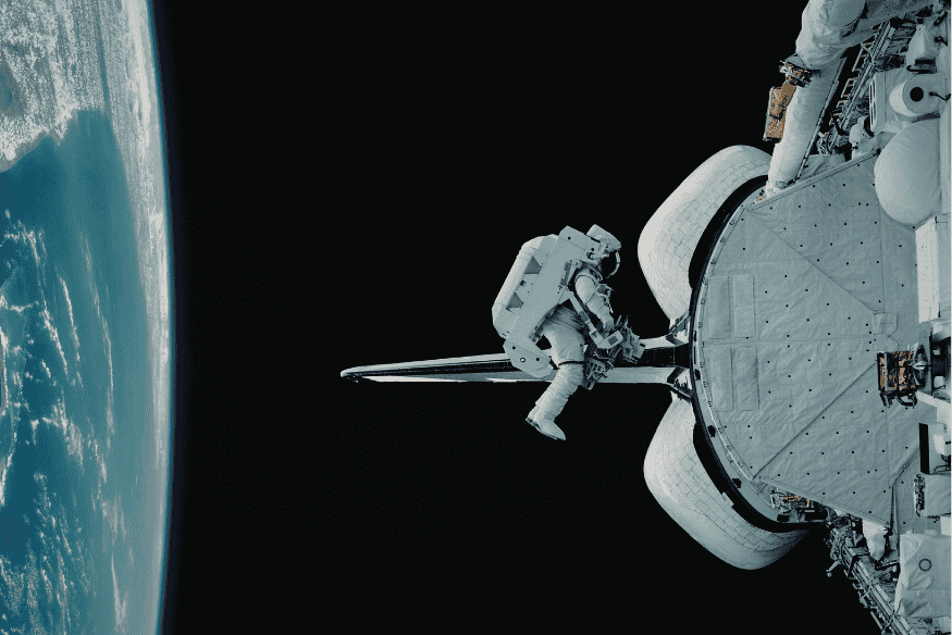 Astronauta realizando caminhada espacial ao lado de nave em órbita da Terra