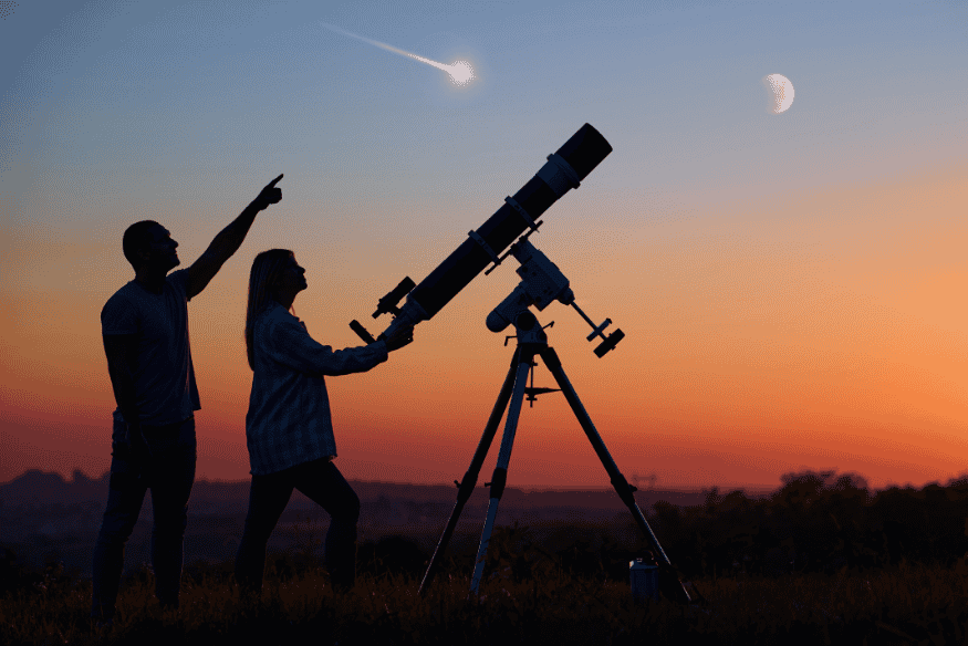 Pessoas usando telescópio ao entardecer para observar objeto brilhante no céu próximo à Lua