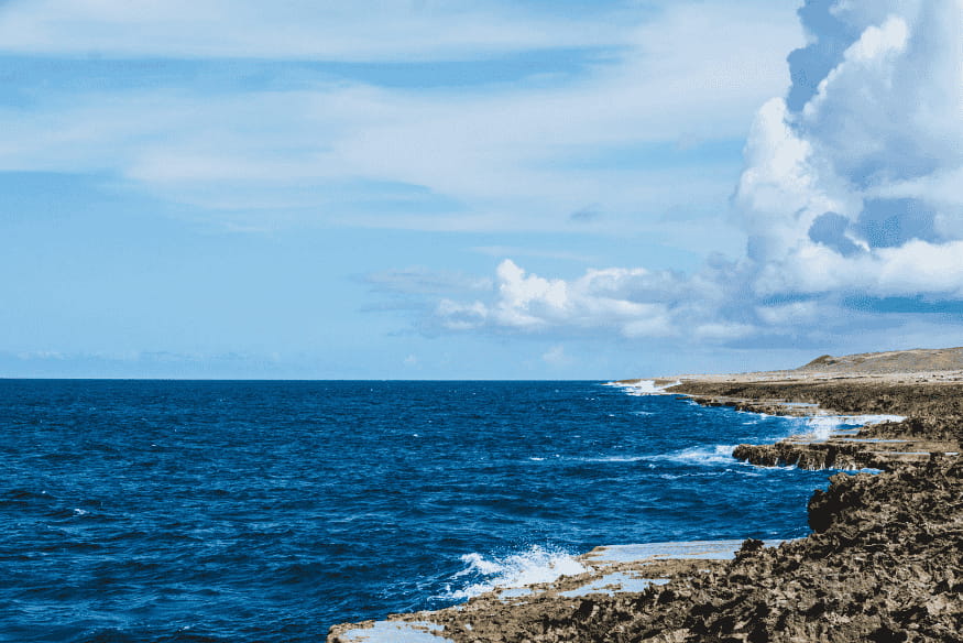 Oceano e costa rochosa sob céu claro, cenário usado para explicar como duas luas poderiam alterar as marés da Terra