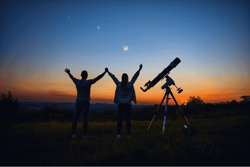 Pessoas observando o céu ao entardecer com telescópio em área aberta, avaliando a qualidade do céu para astrofotografia pela Escala de Bortle