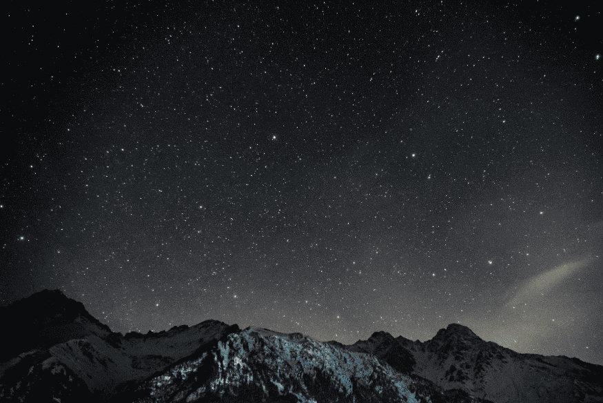 Céu estrelado sobre montanhas durante a noite, cenário ideal para escolher uma estrela brilhante e fazer foco preciso na astrofotografia