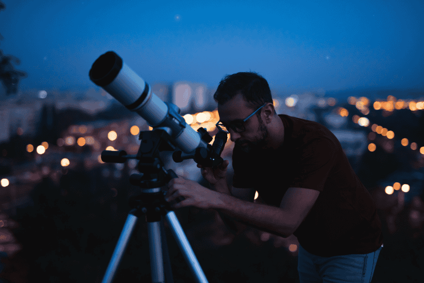 Pessoa ajustando telescópio em tripé durante observação noturna, buscando foco perfeito para fotografar estrelas