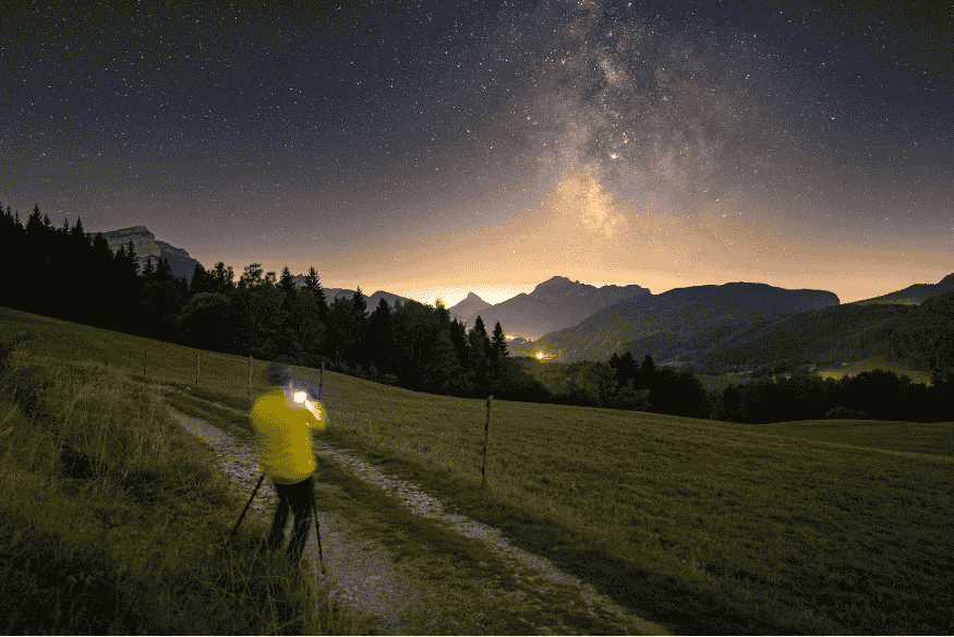 Fotógrafo registrando a Via Láctea em paisagem montanhosa com câmera em tripé e lente grande angular