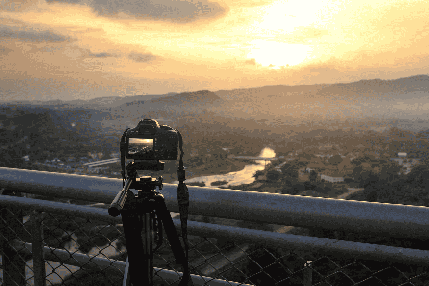 Câmera em tripé fotografando a paisagem ao entardecer, configuração útil para capturar o céu com lente grande angular