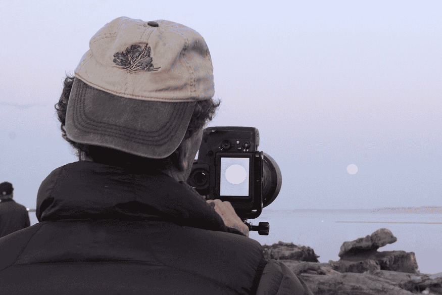 Pessoa fotografando a Lua próxima ao horizonte para registrar o efeito visual da ilusão lunar