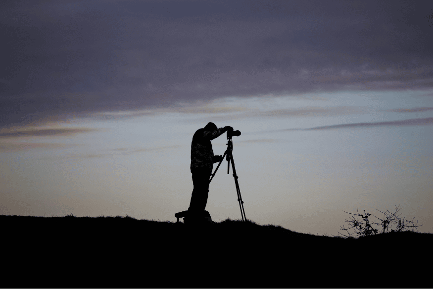 Pessoa usando câmera em tripé ao ar livre, mostrando a importância do tripé em um kit de observação astronômica barato