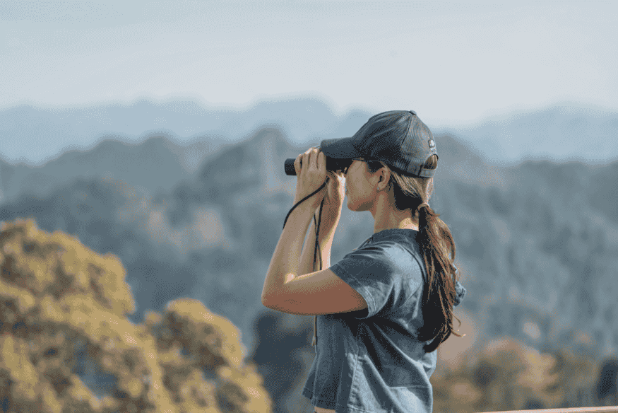 Pessoa observando paisagem com binóculo, equipamento acessível para iniciar na observação astronômica
