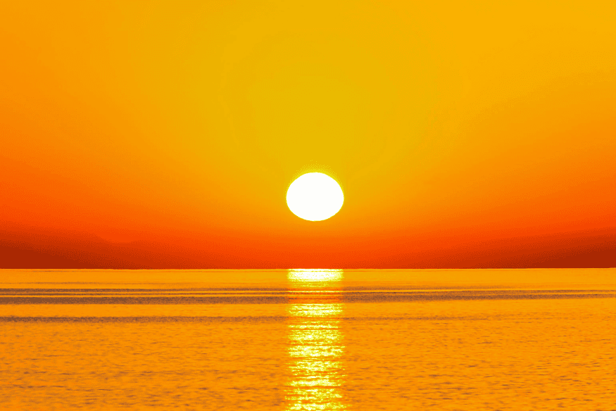 Sol baixo no horizonte sobre o mar com céu alaranjado, exemplo de espalhamento da luz na atmosfera que também influencia a cor da Lua em certas noites