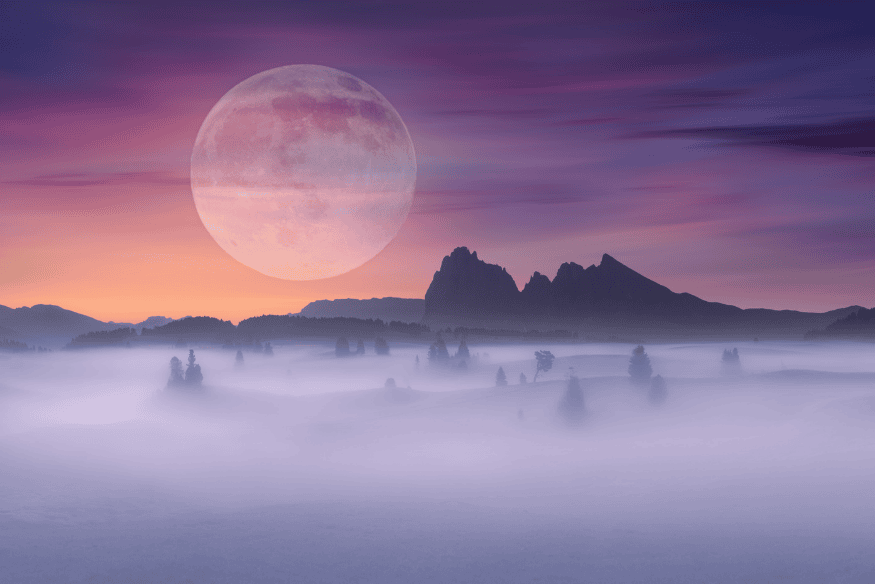 Lua grande e amarelada sobre paisagem com neblina ao amanhecer, mostrando como poeira, fumaça e partículas no ar podem alterar a cor aparente da Lua