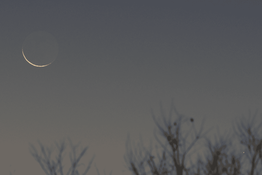 Lua crescente fina no céu com a parte escura suavemente visível, exemplo do fenômeno da luz cinérea