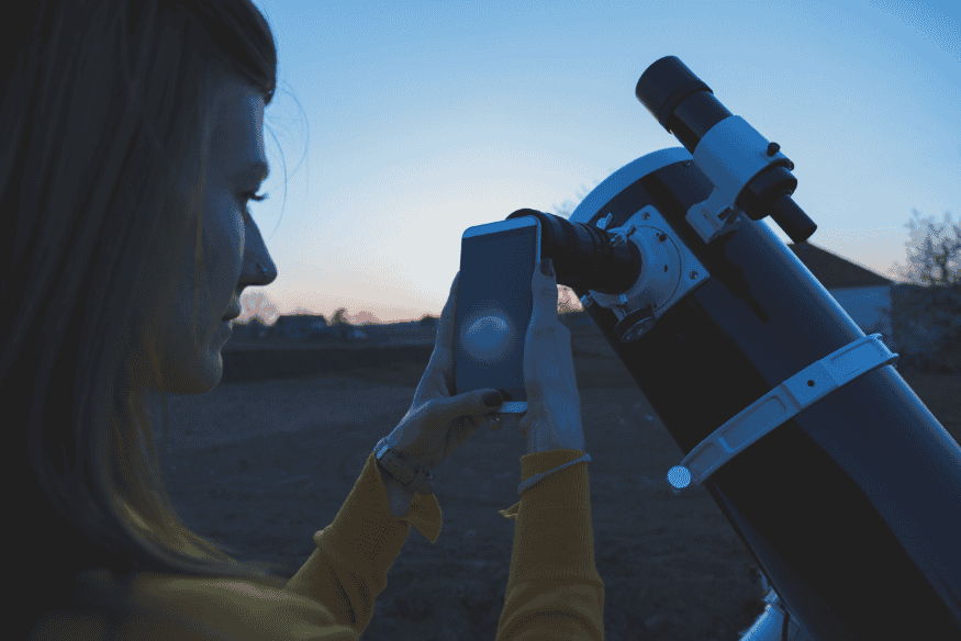 Pessoa observando e fotografando a Lua crescente com telescópio ao entardecer durante a busca pela luz cinérea