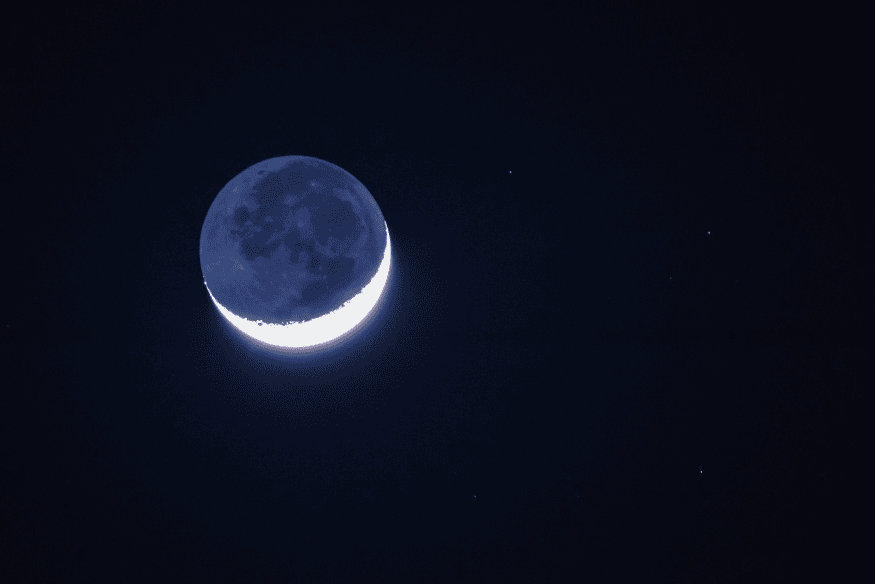 Lua crescente com brilho suave na parte escura observado no céu noturno, característica típica da luz cinérea