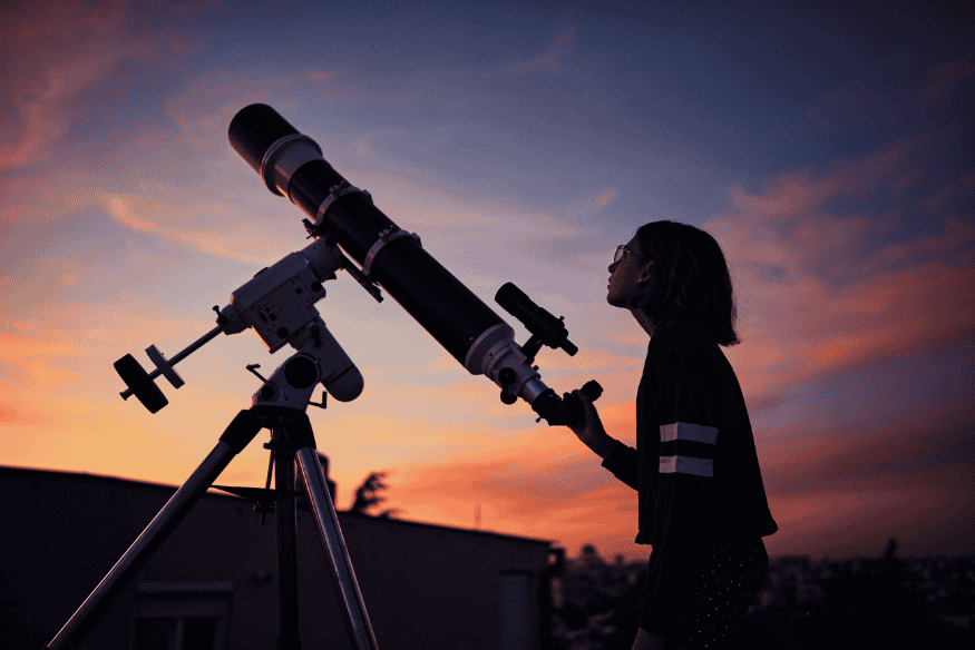 Pessoa ajustando telescópio em montagem equatorial ao entardecer, preparação para observar e fotografar o céu