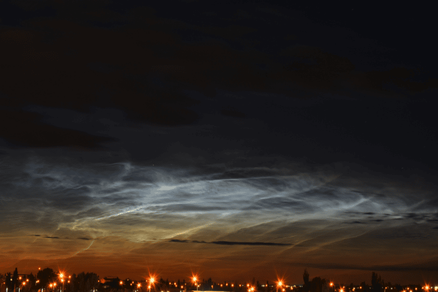 Nuvens noctilucentes luminosas sobre cidade ao anoitecer com brilho prateado no céu