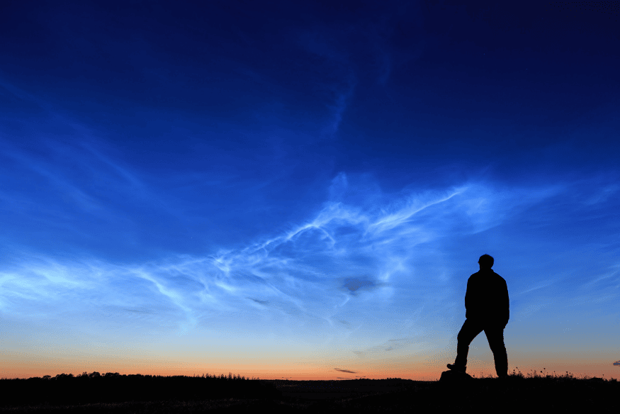 Pessoa observando nuvens noctilucentes brilhando no céu azul ao entardecer