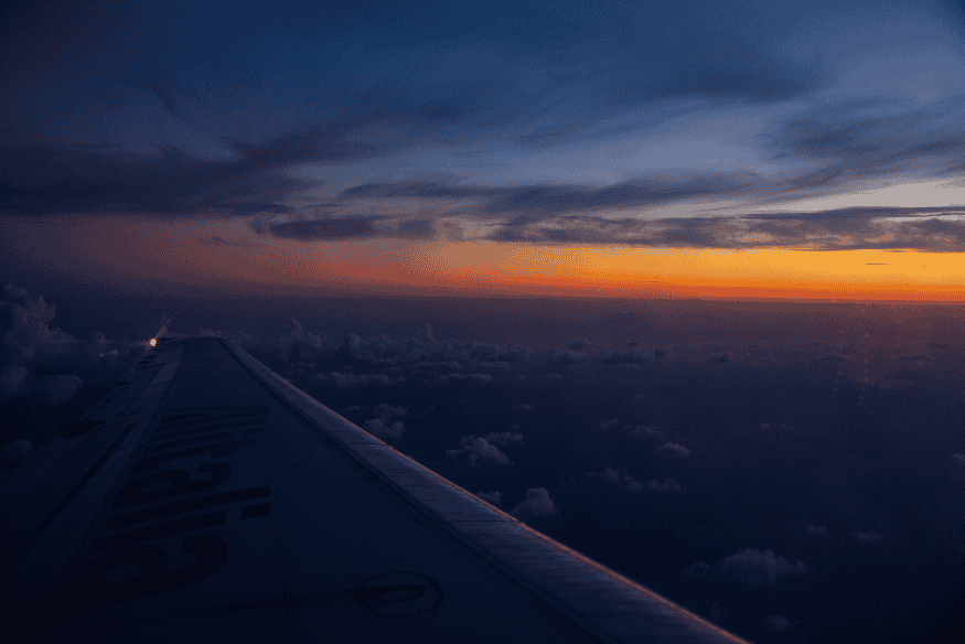 Céu ao entardecer visto da janela de um avião, cenário que ajuda a observar o brilho natural da atmosfera