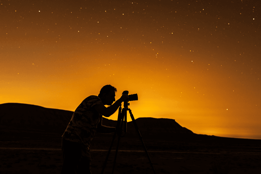 Pessoa usando câmera em tripé sob céu estrelado, situação em que o controle de orvalho é essencial para proteger o equipamento