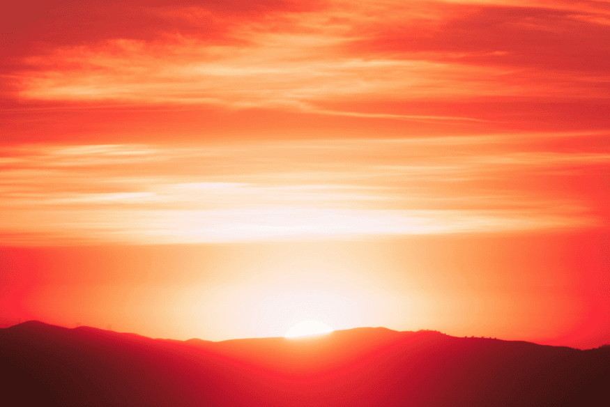 Sol se pondo atrás de montanhas em tons vermelhos, exemplo de como a atmosfera pode intensificar as cores do entardecer