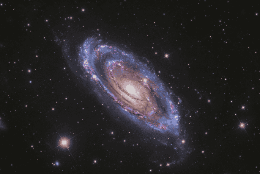 Galáxia espiral com braços luminosos e regiões azuladas associadas à formação de estrelas