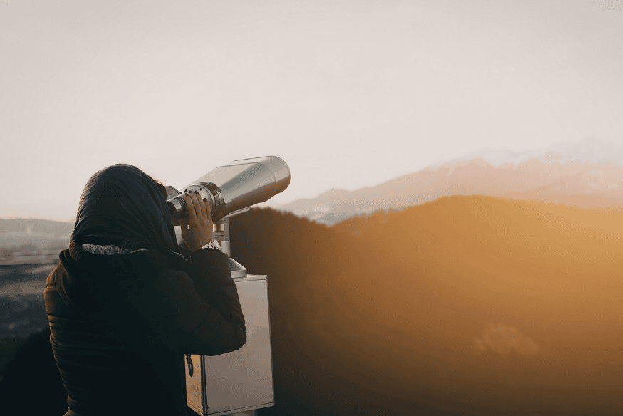 Pessoa usando luneta de observação ao pôr do sol, representando a busca por boa qualidade de imagem em equipamentos astronômicos