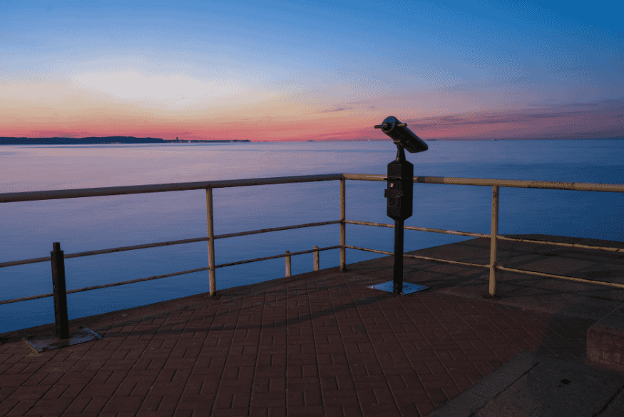 Luneta de observação fixa em mirante à beira-mar ao entardecer, ilustrando a escolha de telescópio para observação prática