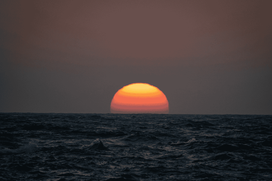 Sol parcialmente oculto no horizonte oceânico, mostrando mudança de cor e percepção visual ao pôr do sol