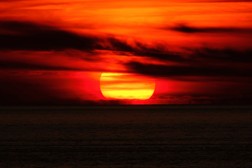 Sol vermelho próximo ao horizonte sobre o mar, exemplo da ilusão visual que faz o Sol parecer maior