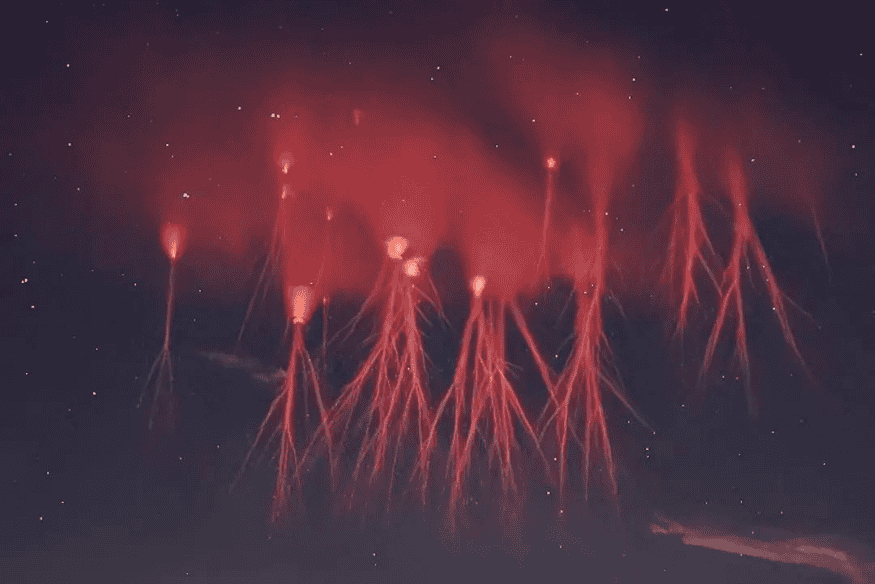 Sprites vermelhos no céu noturno com estruturas alongadas e ramificadas acima de uma tempestade
