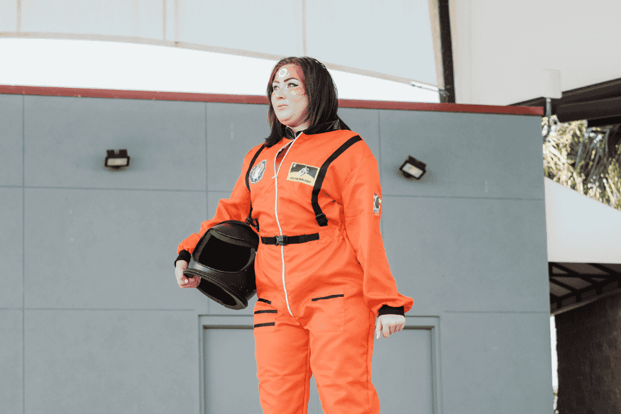Pessoa vestida com traje espacial segurando capacete, representação da importância do equipamento de proteção para sobreviver no espaço