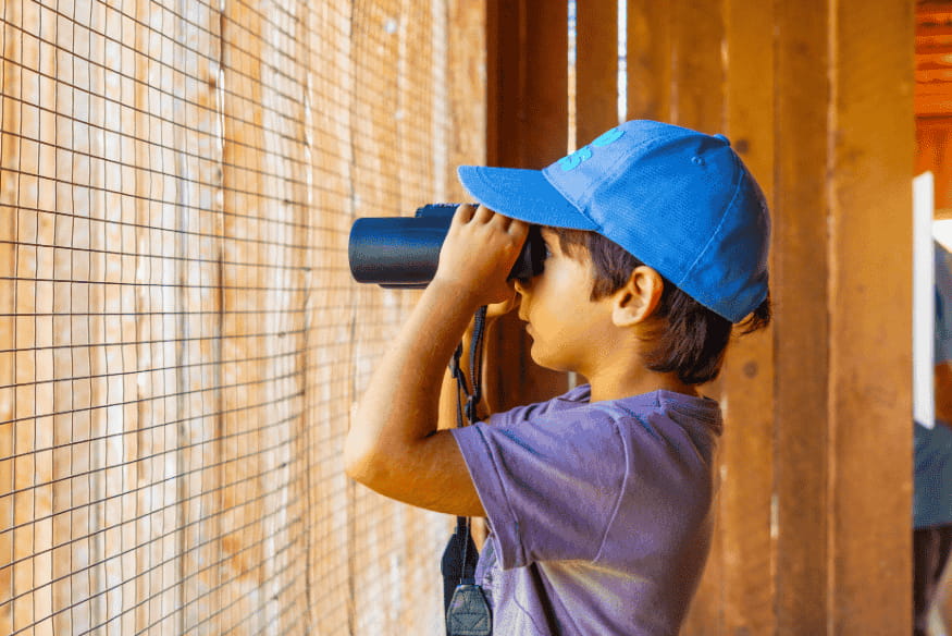 Criança observando com binóculo durante o dia, exemplo de iniciação à astronomia visual e à observação do céu com equipamento simples