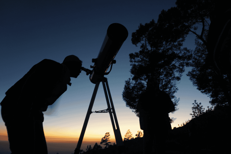 Pessoa observando pelo telescópio ao anoitecer, representando a experiência da astronomia visual focada em contemplação e observação direta do céu