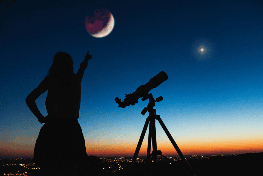 Silhueta de pessoa ao lado de telescópio apontando para a Lua no crepúsculo, ilustrando a decisão entre observação visual e astrofotografia na astronomia amadora