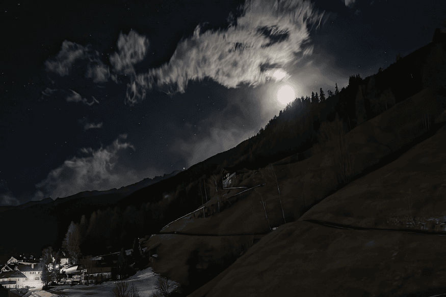 Paisagem noturna em região de serra com céu escuro, nuvens e brilho da Lua atrás da montanha, exemplo de local elevado para observar a Via Láctea
