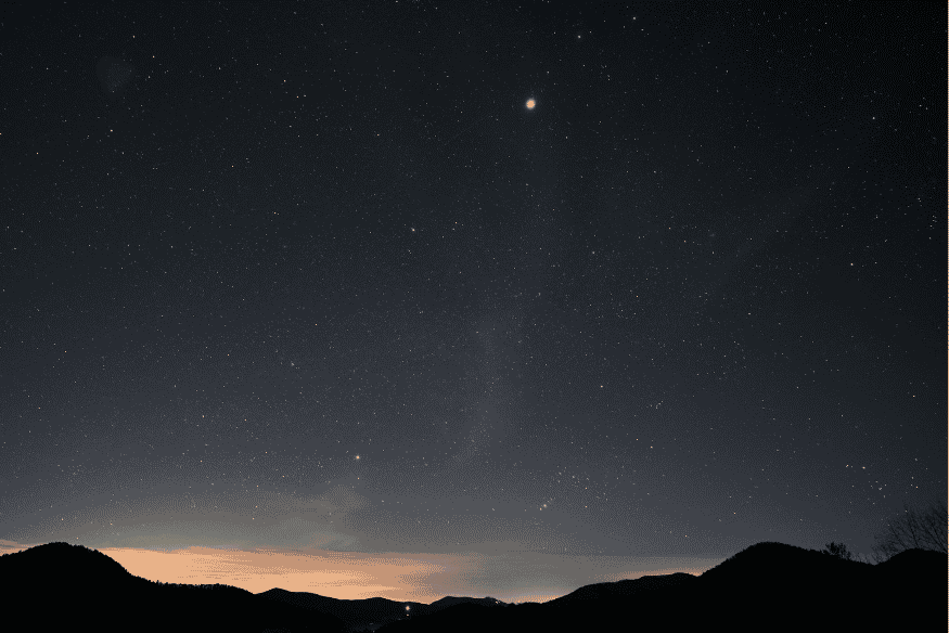 Céu noturno com pontos brilhantes se movendo entre estrelas sobre montanhas