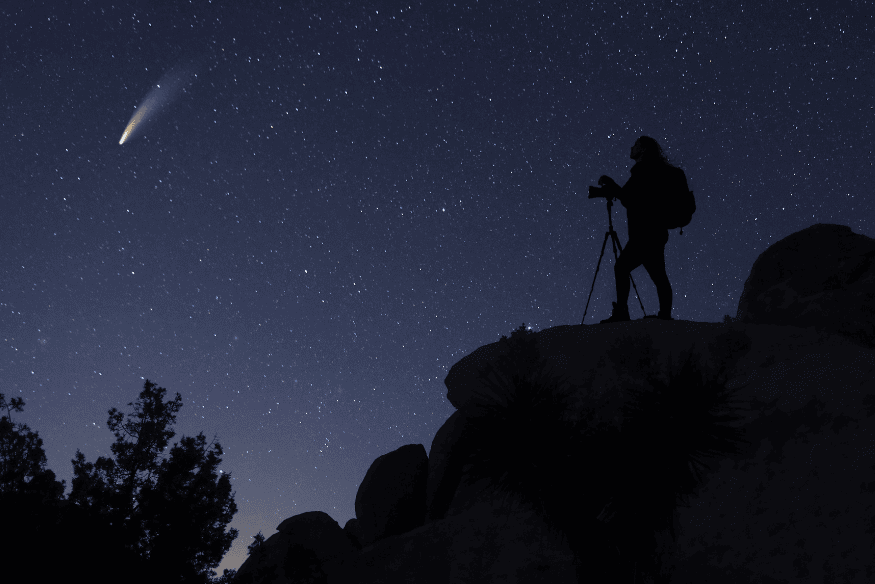 Fotógrafo em silhueta registrando um cometa no céu noturno, exemplo de cena astronômica que ganha contraste e definição com bom pós-processamento na astrofotografia